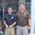Andy Goldstein, Managing Partner of Potomac Pizza, in a brown shirt, khaki shorts and a smile stands with Target Community participant Adam T. in a blue shirt and khaki shorts.