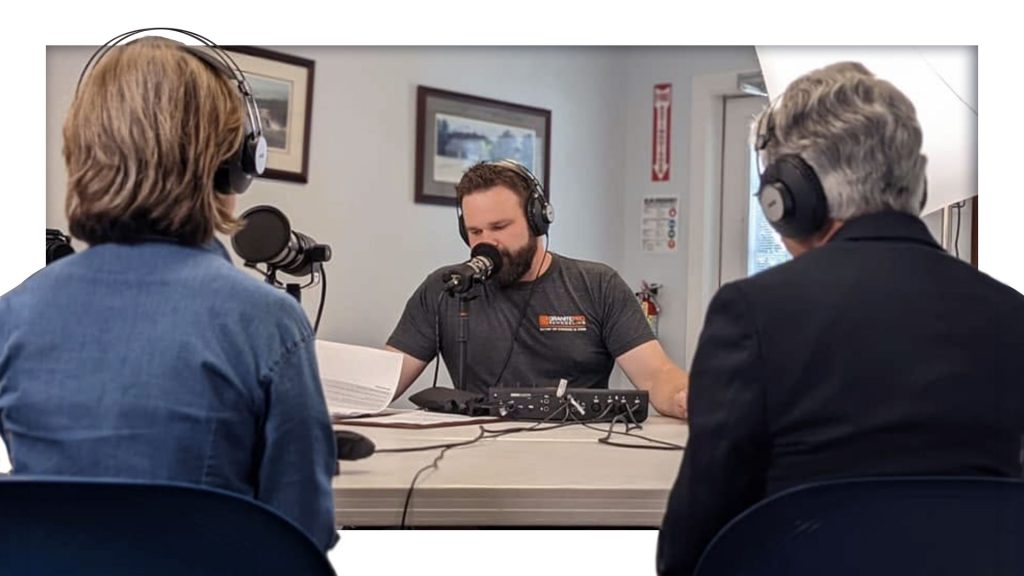 A podcast host records an interview with two guests seated across the table, each speaking into microphones while wearing headphones in a podcast studio.